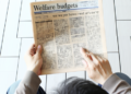 An individual reading a newspaper article about welfare budgets